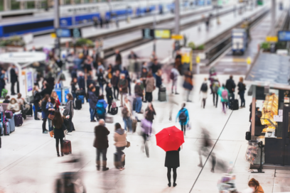 Une foule de personnes dans un hall de gare, l'une d'elles porte un parapluie rouge