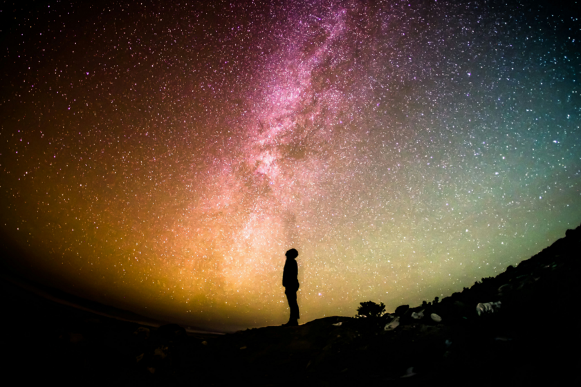 Un homme de profil, debout, regarde au-dessus de lui un ciel étoilé et coloré